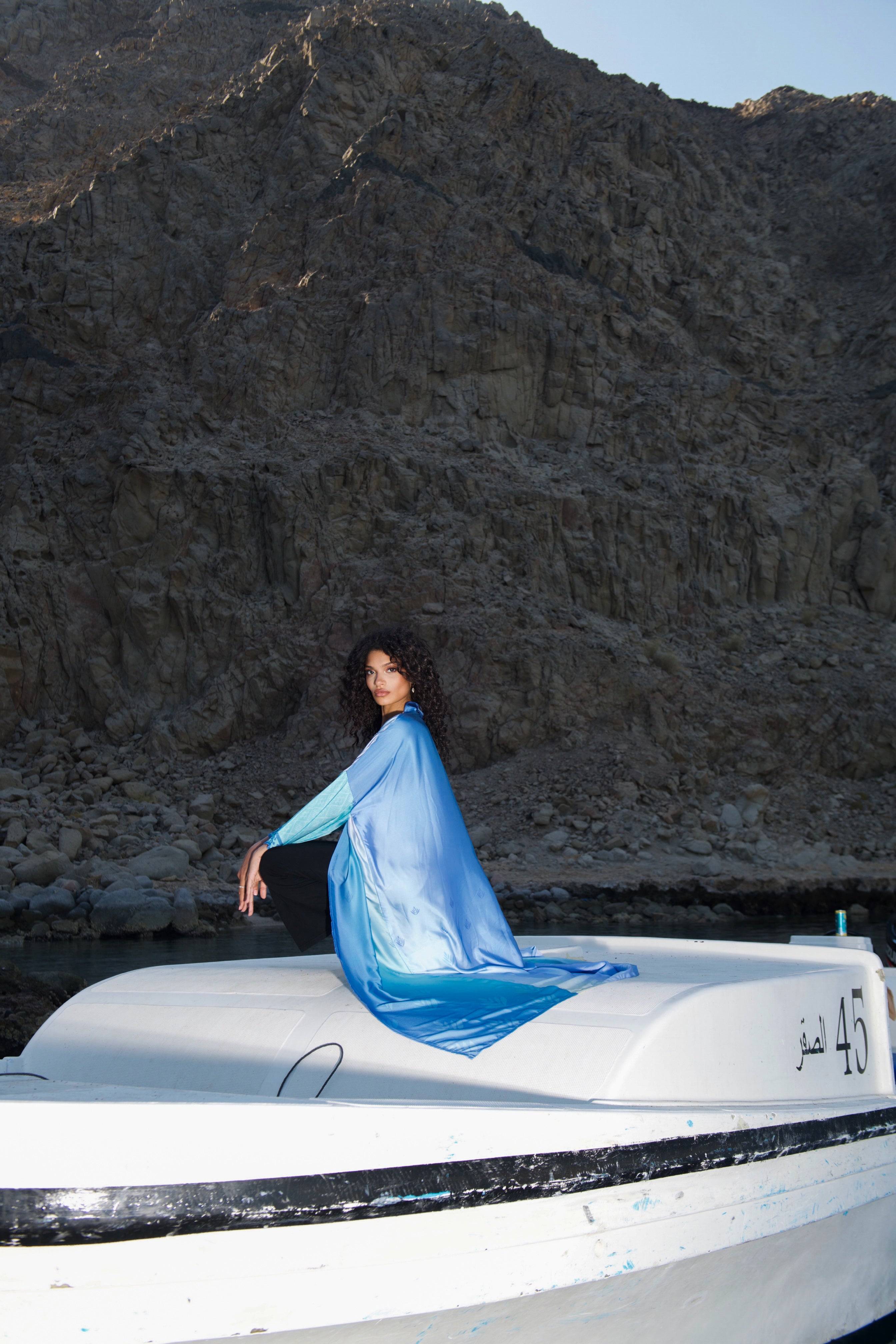 Shop the Indigo Dream Ombré Abaya Set, draped elegantly on a boat with a serene mountain backdrop, highlighting its breezy, luxurious texture.