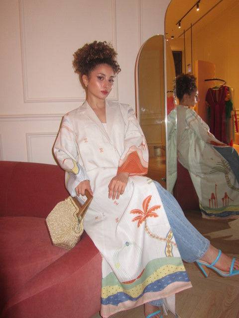 Model seated on ottoman in The Jeddah Horizon - Abaya & Scarf Set, showcasing the garment’s bold sleeve and skirt prints.