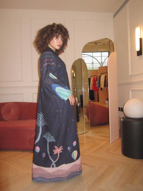 Side view of The Alula Horizon Blazer Abaya with vibrant sleeve and hemline prints, styled in a modern indoor space.