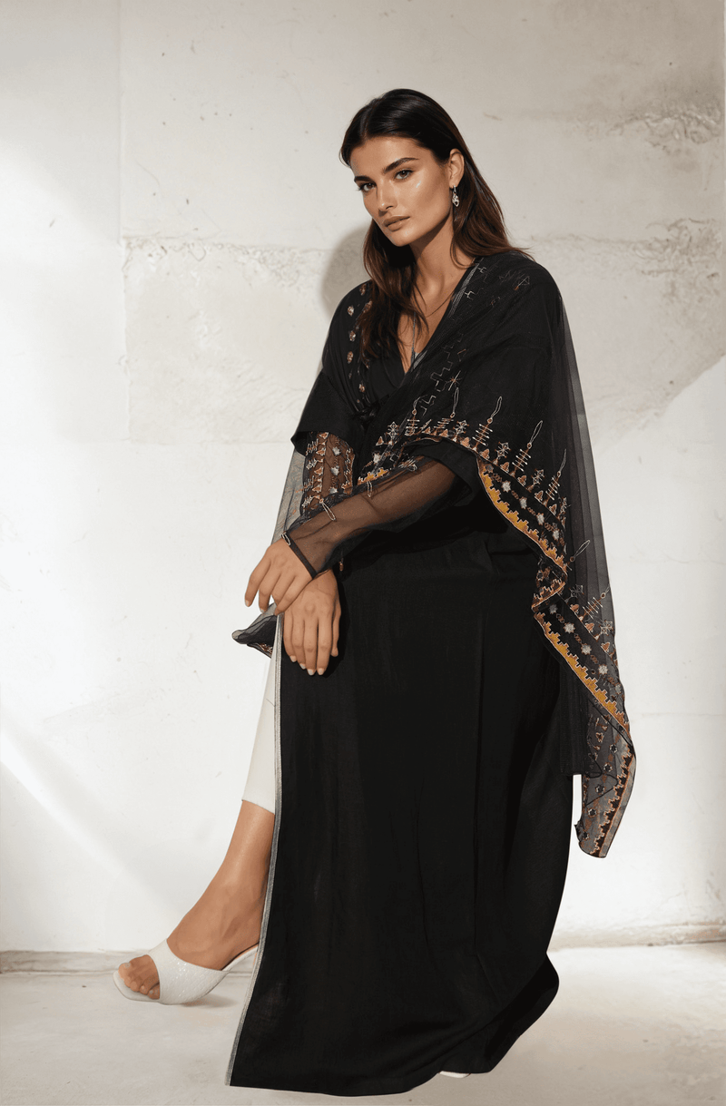 Seated model in Saudi Abaya & Scarf Set with embroidered sheer overlay, combining traditional design with modern elegance.