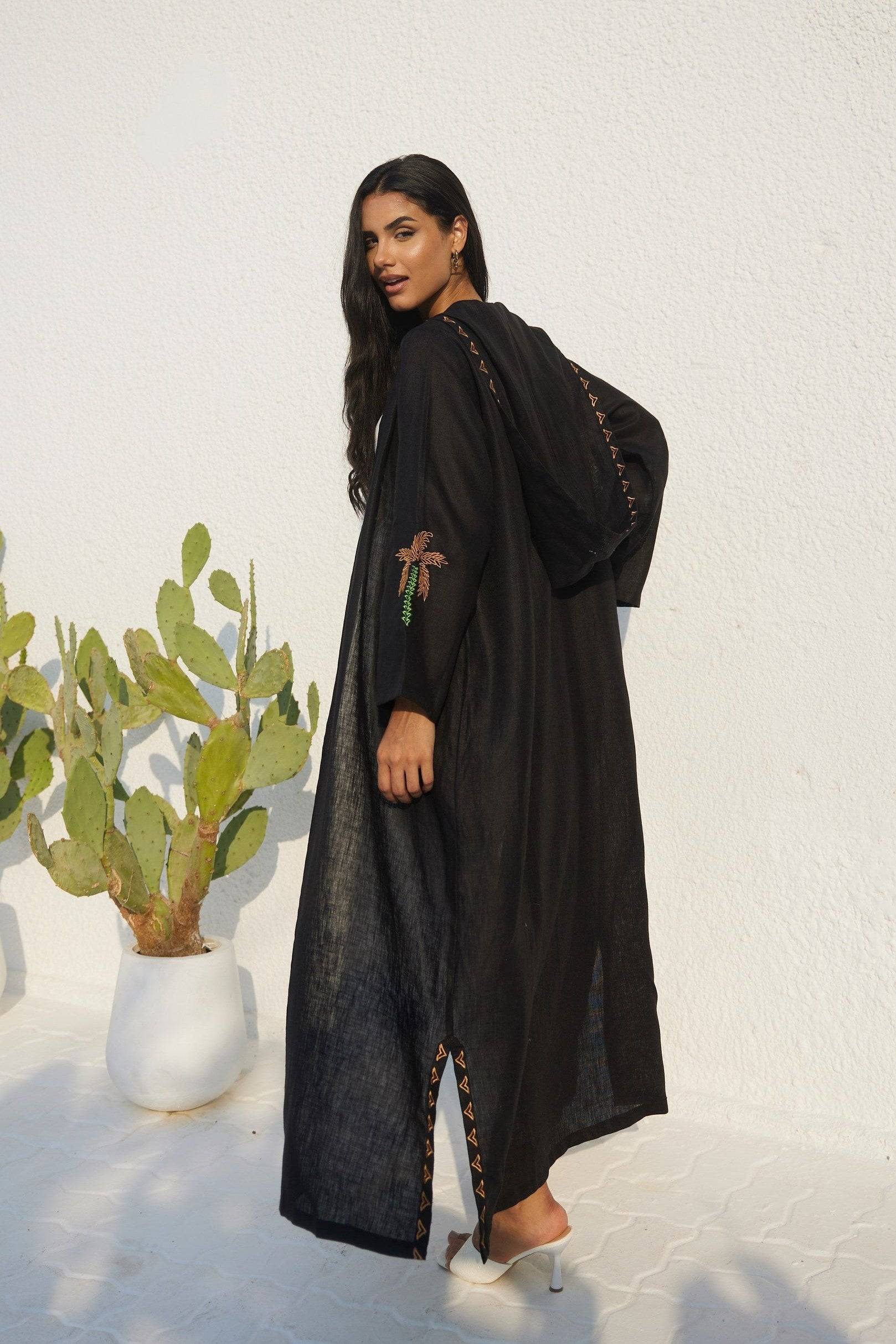 Model in Nakhla Hoodie Abaya turning back, showcasing hood and sleeve embroidery. Made from eco-friendly organic linen.