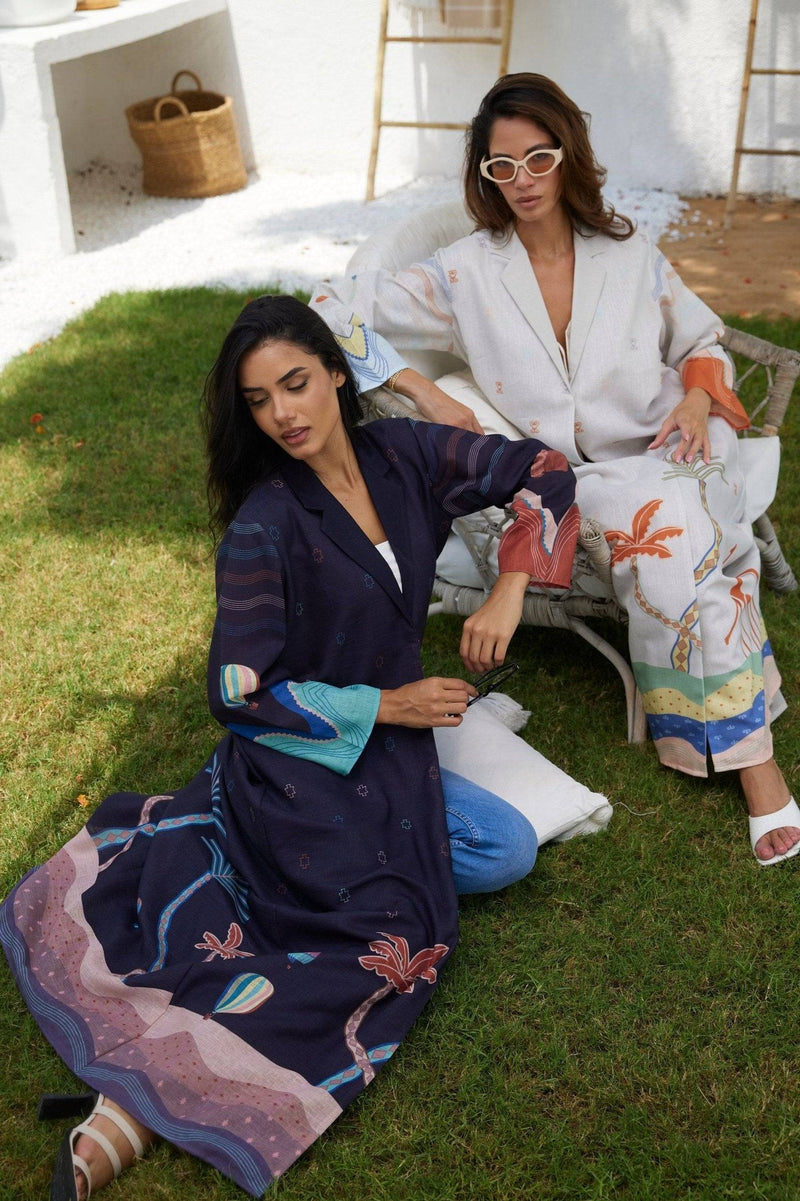 Models lounging in navy and white Alula Horizon Blazer Abayas, highlighting the garment's artistic desert-themed prints.