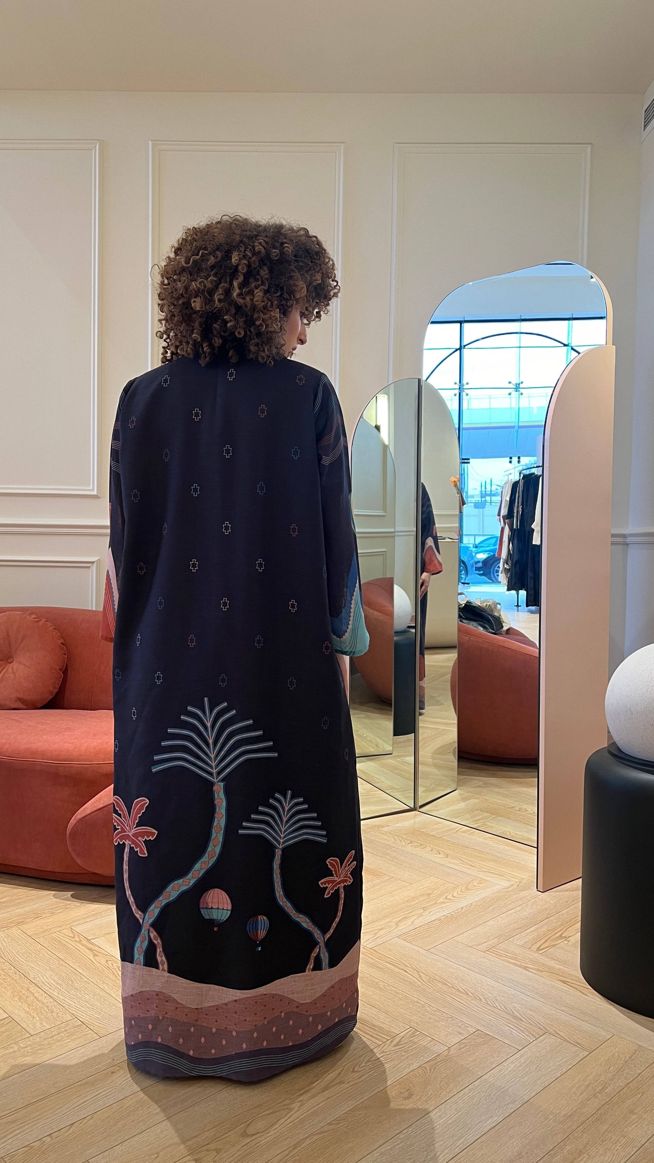 Back view of The Alula Horizon Blazer Abaya with palm tree and hot air balloon prints, styled in a boutique setting.
