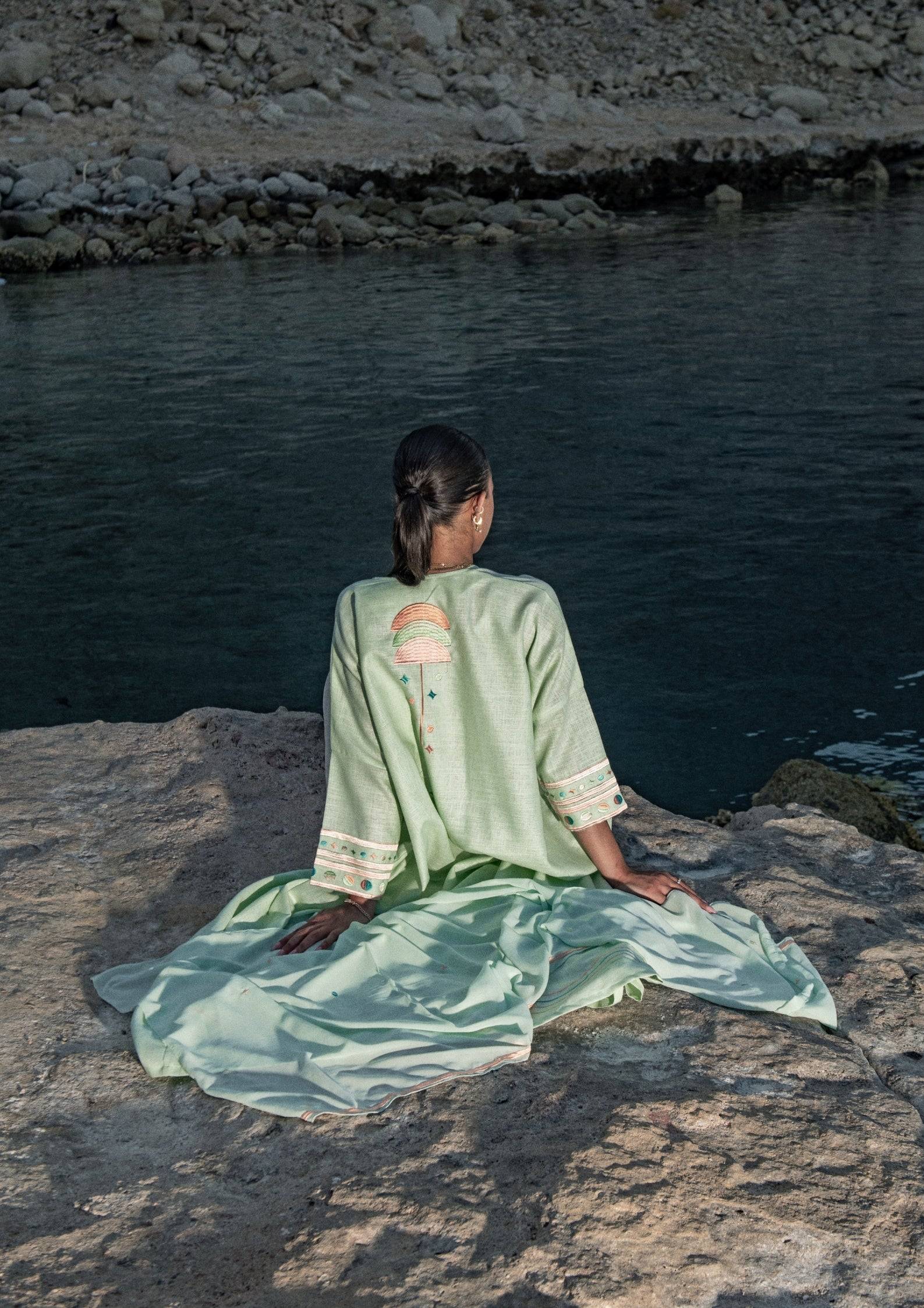 Cold mint Birthday Abaya with scarf, worn outdoors near water, highlighting relaxed fit and intricate back embroidery.