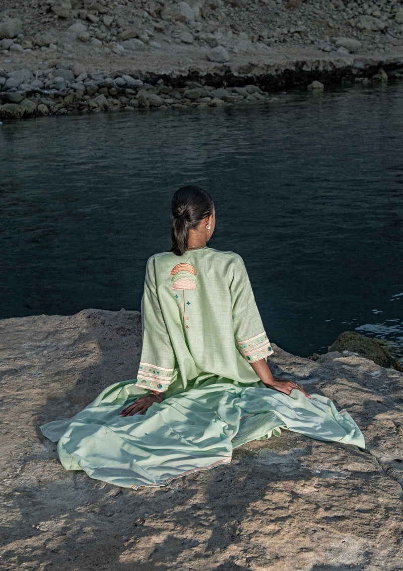 Cold mint Birthday Abaya with scarf, worn outdoors near water, highlighting relaxed fit and intricate back embroidery.