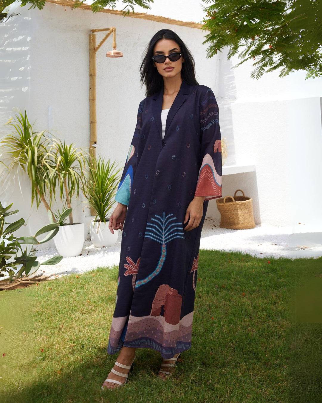 Elegant navy Alula Horizon Blazer Abaya with desert motifs and palm tree prints, styled outdoors with heels for a modern traditional look.