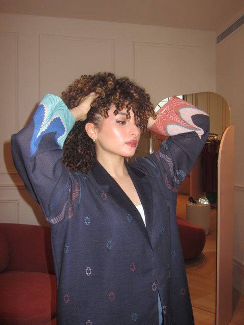 Close-up of model adjusting hair in The Alula Horizon Blazer Abaya, showcasing detailed sleeve patterns and linen texture.