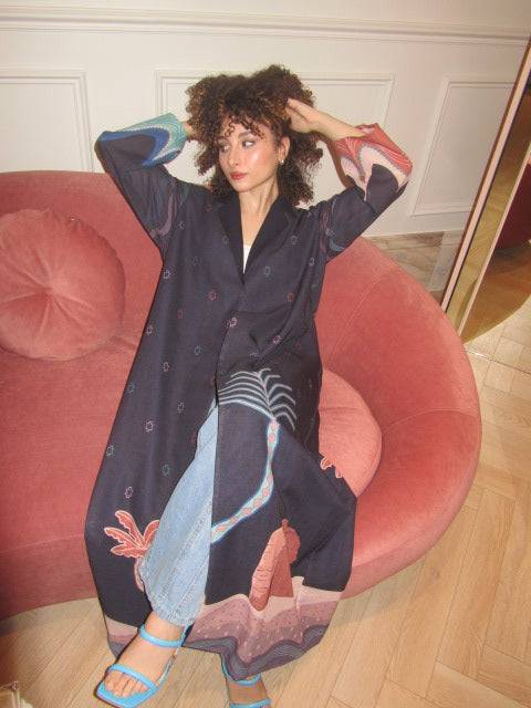 Model seated in The Alula Horizon Blazer Abaya, showing off the artistic desert landscape design and relaxed fit.