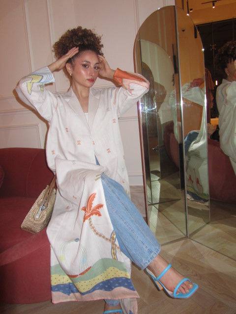 Model seated in The Jeddah Horizon - Abaya & Scarf Set paired with jeans and blue sandals, showing off hemline design.