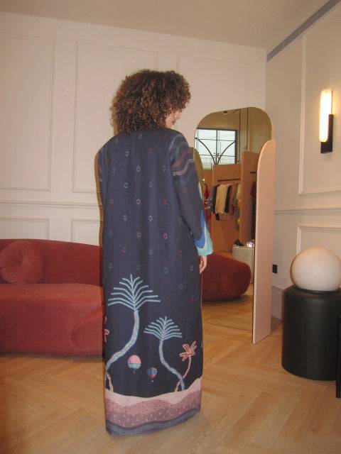 Model in boutique wearing The Alula Horizon Blazer Abaya, highlighting the back design with desert and palm tree prints.