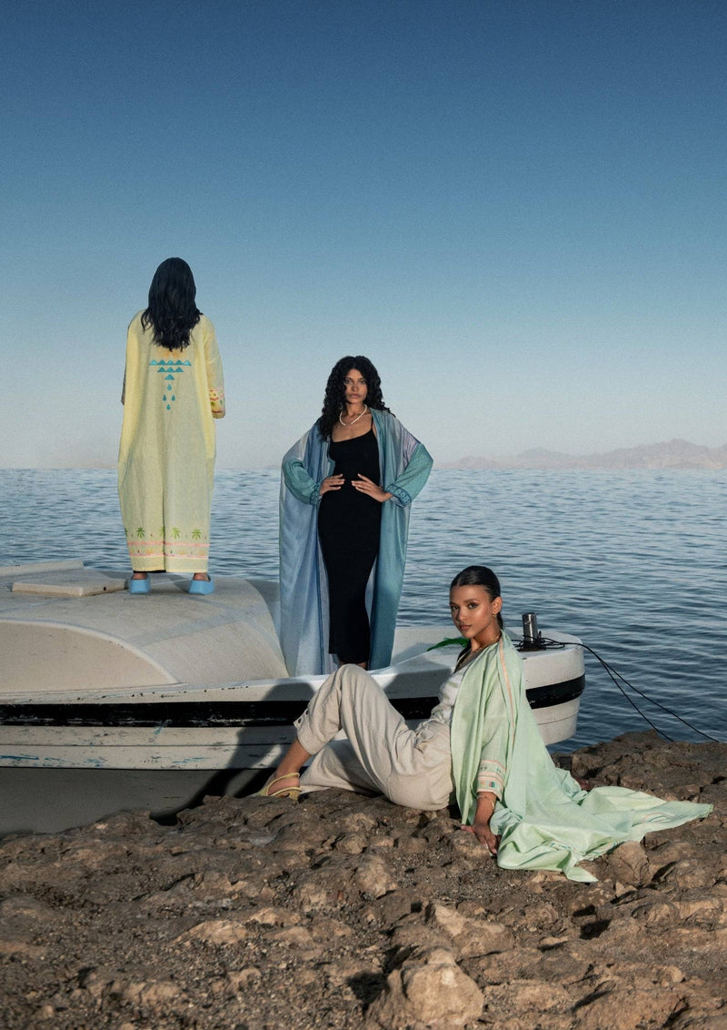 Three women in vibrant abayas by the water, highlighting the cold mint Birthday Abaya & Scarf Set as a standout summer piece.