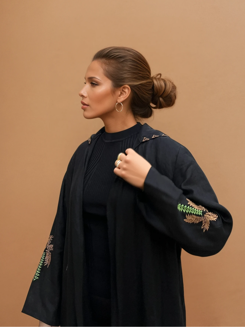 Nakhla Hoodie Abaya in organic linen with palm embroidery on sleeves, styled with hoop earrings. Features hidden pockets and a relaxed fit.