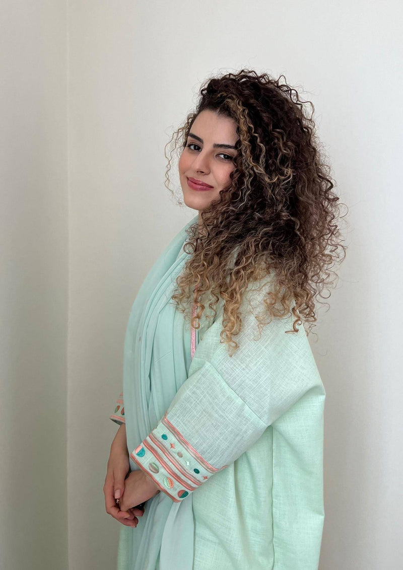 Side profile of model in cold mint Birthday Abaya, highlighting relaxed fit and colorful sleeve embroidery.