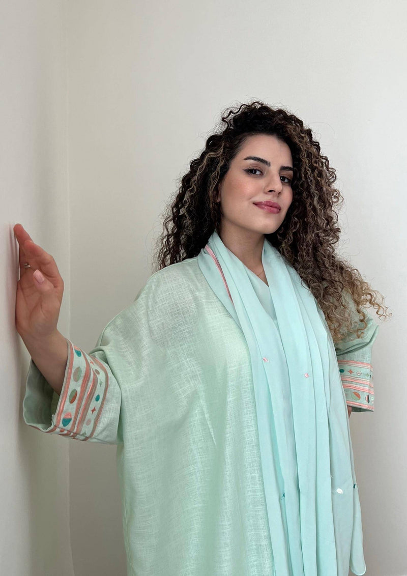 Model indoors wearing cold mint Birthday Abaya & Scarf Set, showcasing soft fabric and pastel embroidered cuffs.