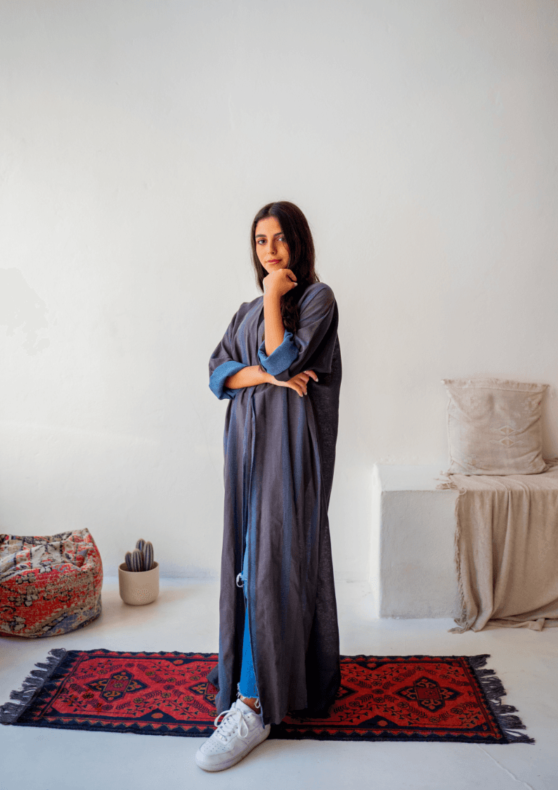 The WORKaholic Abaya - Daily Wear in dark grey with blue cuffs, styled casually with sneakers on a red patterned rug.
