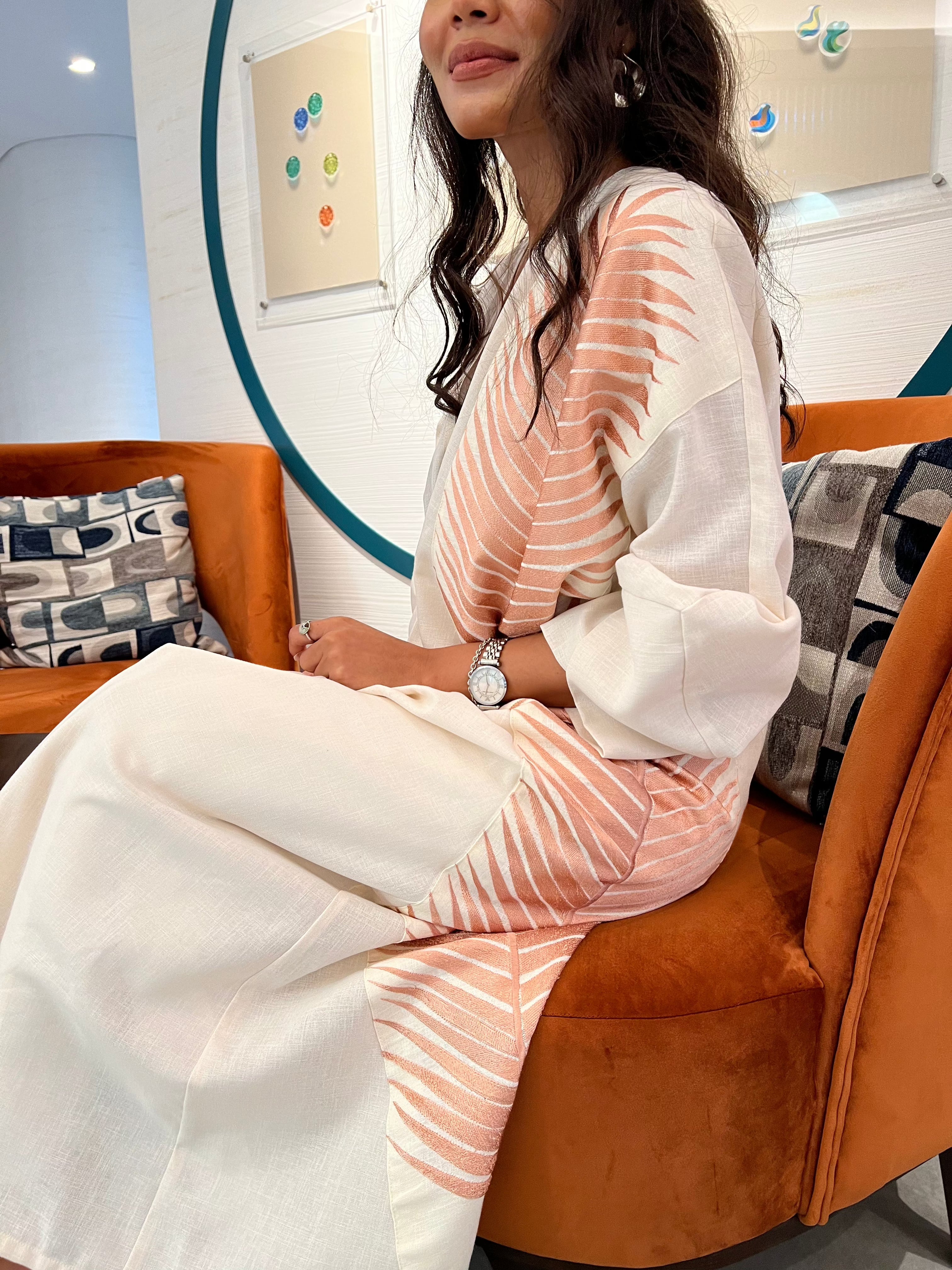 Rosé Gold Abaya - Breast Cancer Awareness | Solidarity, Hope. Seated model showcasing the abaya’s detailed embroidery and soft flowing fabric.