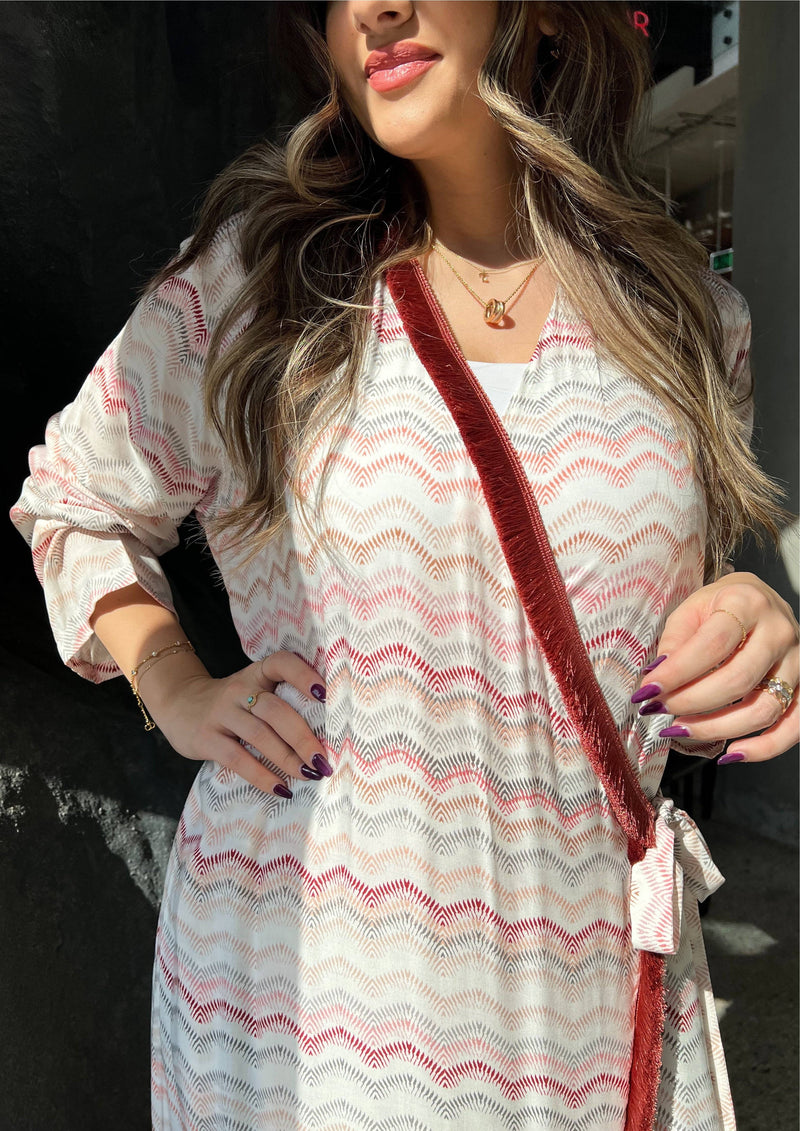 Close-up of pink print wrap abaya with red velvet trim and tie. Soft fabric and elegant design made in Saudi Arabia.