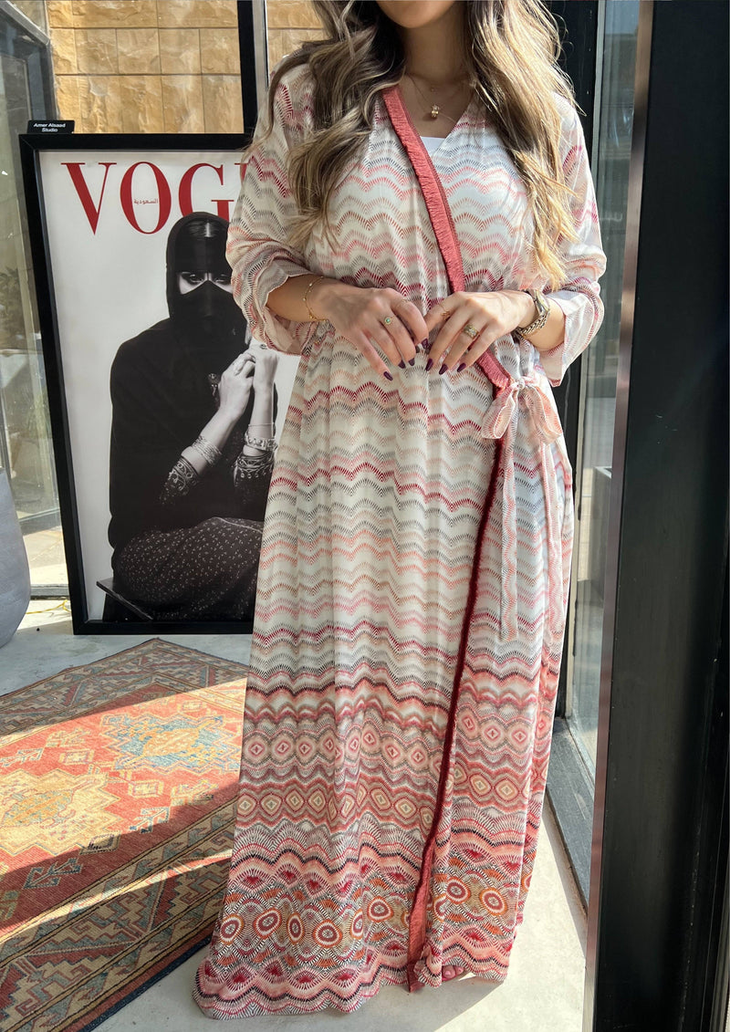 Full-length pink print wrap abaya with geometric patterns and red sash tie. Elegant Saudi-made kimono for casual or formal wear.