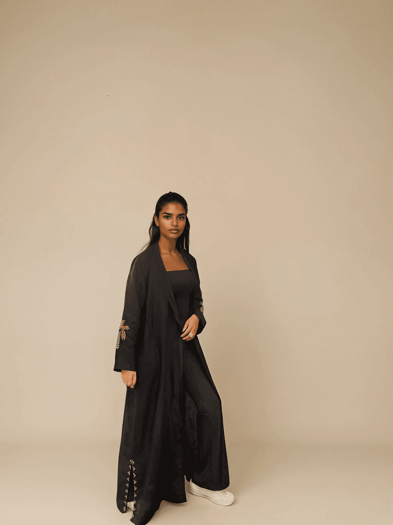 Full-length view of Nakhla Hoodie Abaya in minimalist studio, emphasizing its organic fabric and embroidered sleeves.