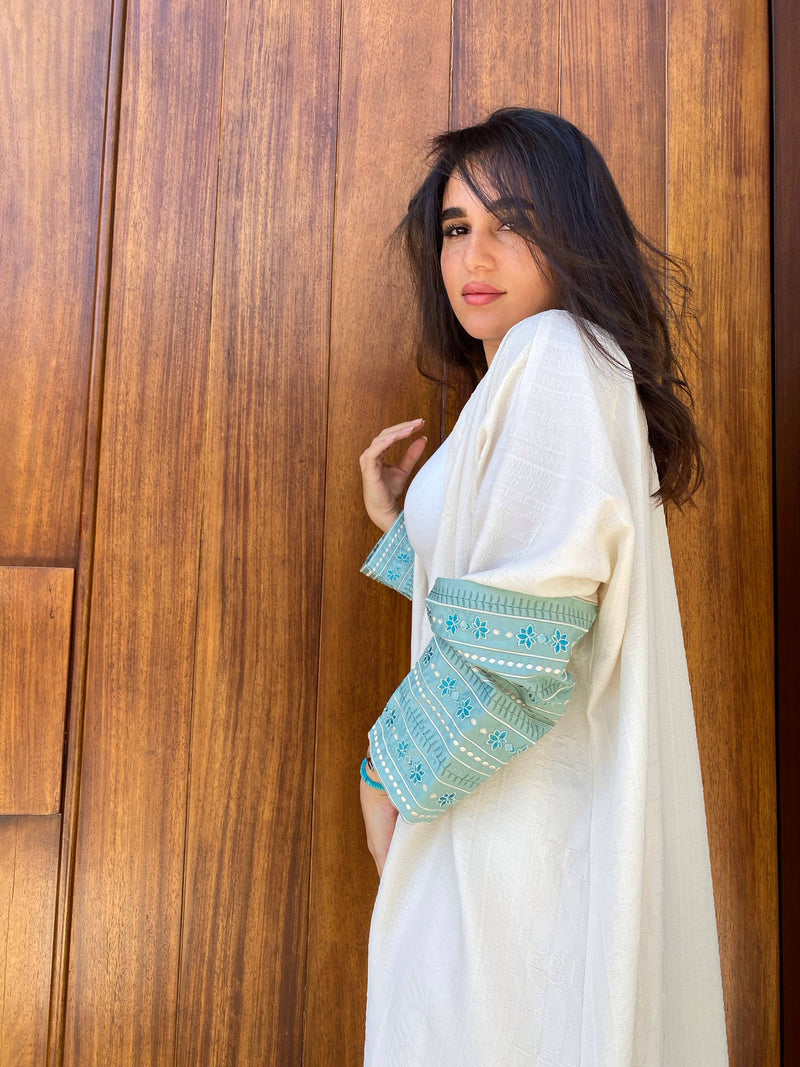L'idée Abaya in ivory with turquoise embroidered sleeves, shown from the side. A refined choice in traditional women's apparel.