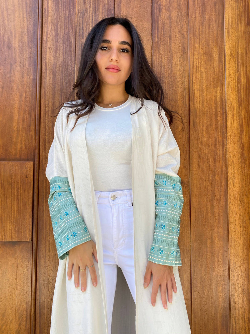 Front view of L'idée Abaya featuring intricate turquoise floral embroidery on long sleeves. Stylish traditional clothing for women.