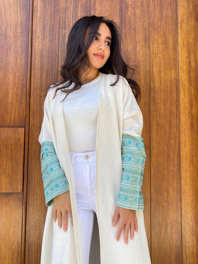 L'idée Abaya with embroidered floral sleeves in turquoise, styled over a white outfit. Elegant traditional wear for modern occasions.