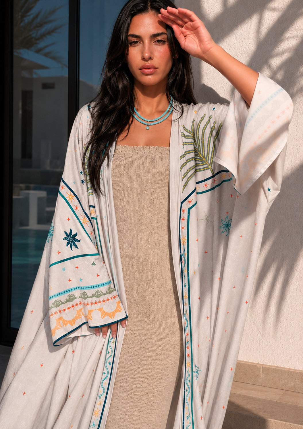 Woman wearing a beige dress with an embroidered white cover-up by a poolside.
