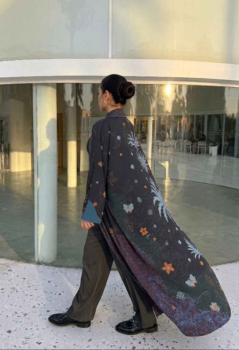 girl wearing a long, patterned cabaya walking in front of a modern building.