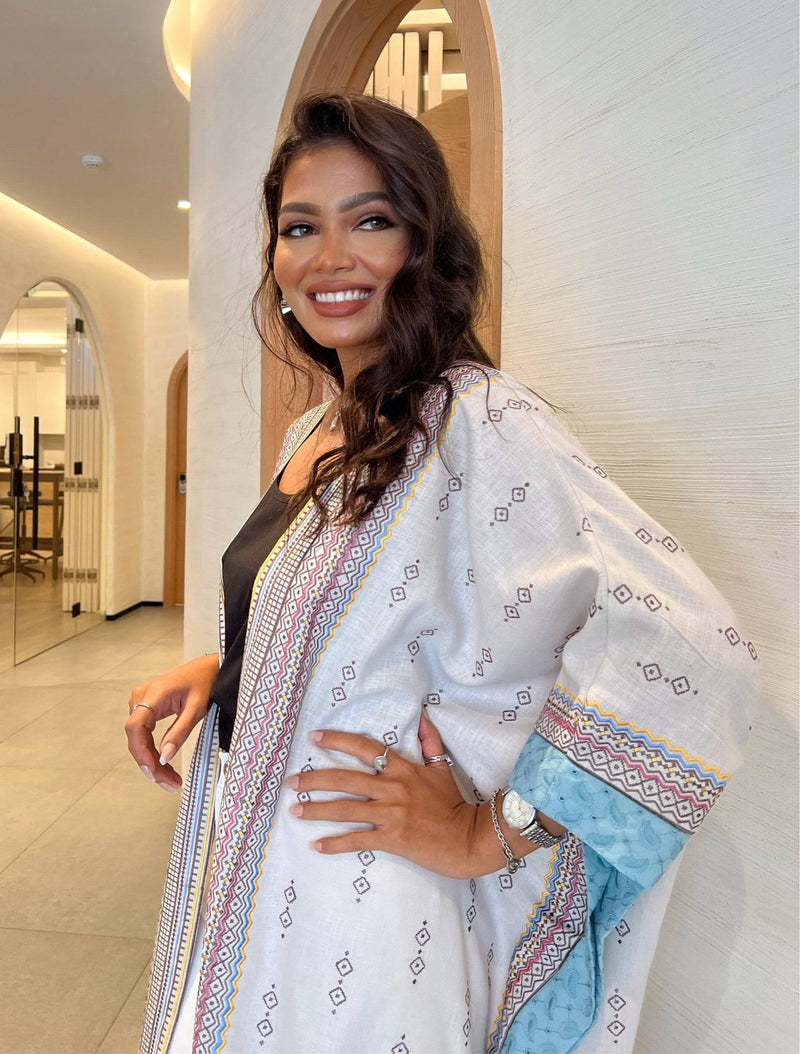 Smiling model in Fatina Abaya with detailed embroidery and blue sleeve lining, styled for a chic indoor setting.